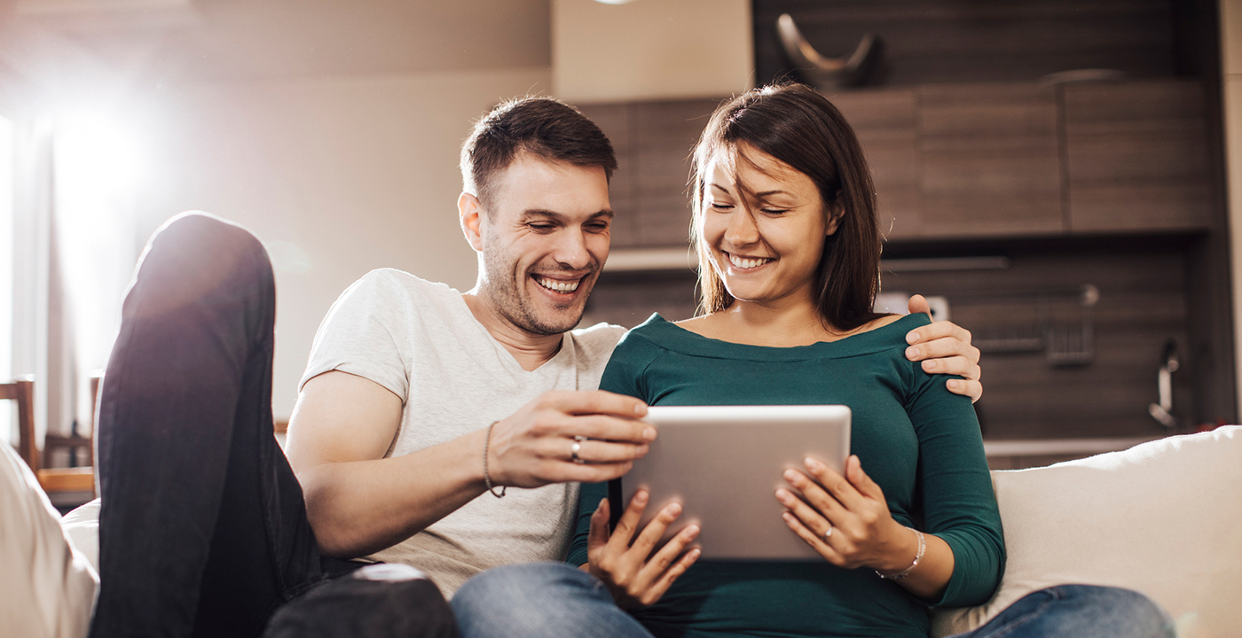 happy pregnant couple looking at tablet