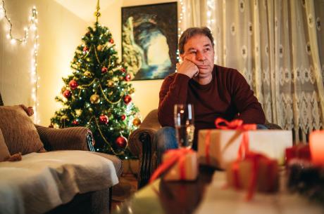 Senior caucasian man sitting on a couch and waiting alone for Christmas / New Year&#039;s eve.