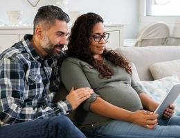 pregnant woman with husband looking at ipad on couch