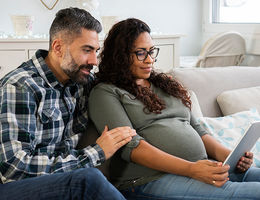 pregnant woman with husband looking at ipad on couch