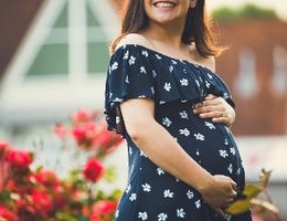 pregnant woman outdoors with her arms around stomach